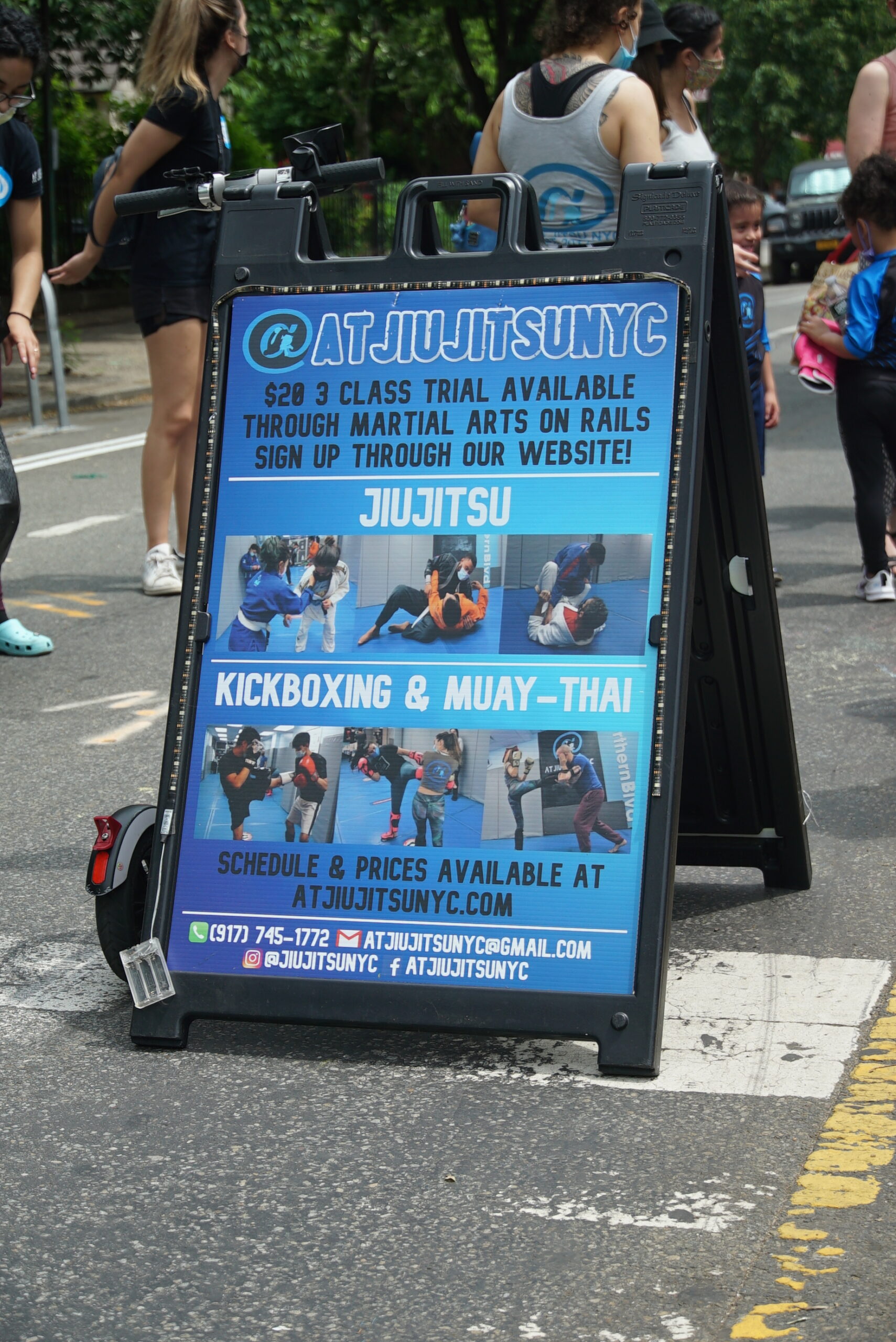 A sandwich board set up next to the class reads, "AT JiuJitsuNYC. $20 3-class trial available through martial arts on rails. Sign up through our website! Jiu jitsu. Kickboxing. Muay thai."