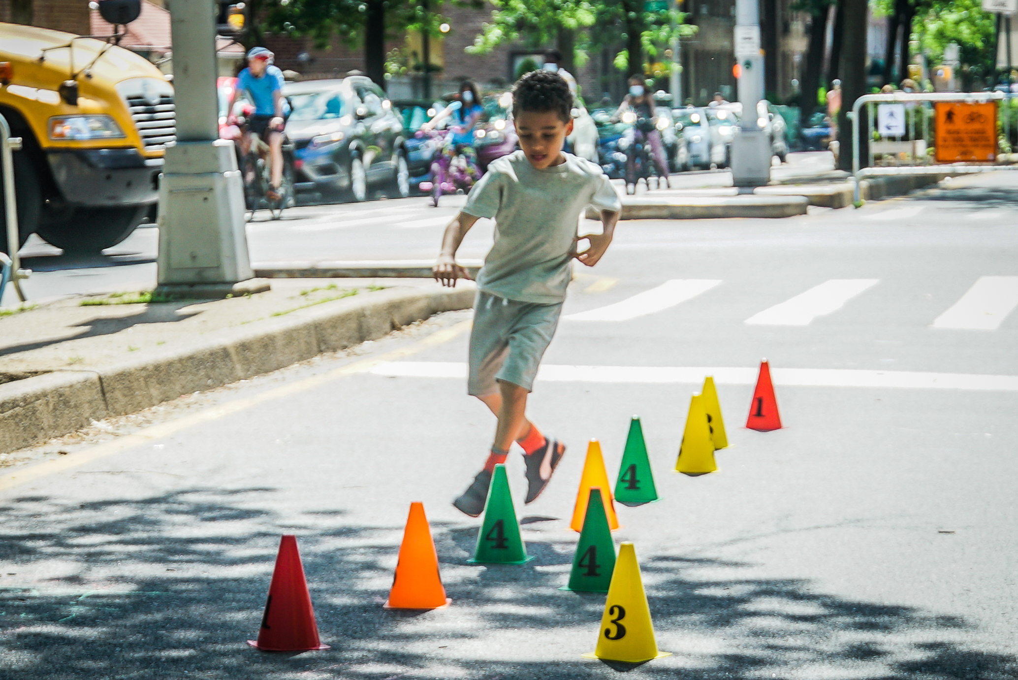 A young boy runs through the obstacle course as part of the Coalition's activities. He is maneuvering between small, colorful cones that have been set up on the street to create the obstacle course