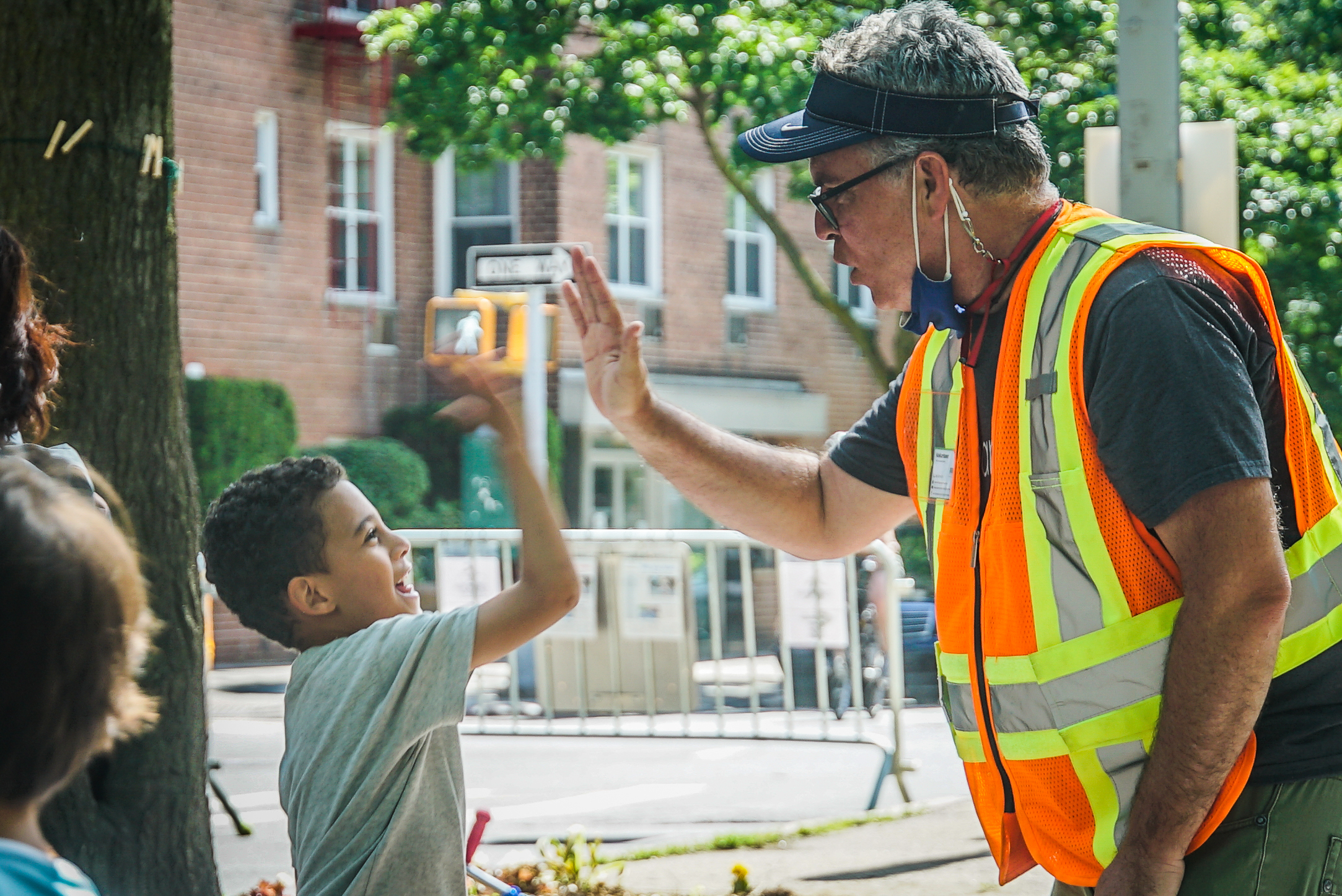 On a sunny day on the Open Street, a young boy with a big smile jumps up to slap Jim a high five.