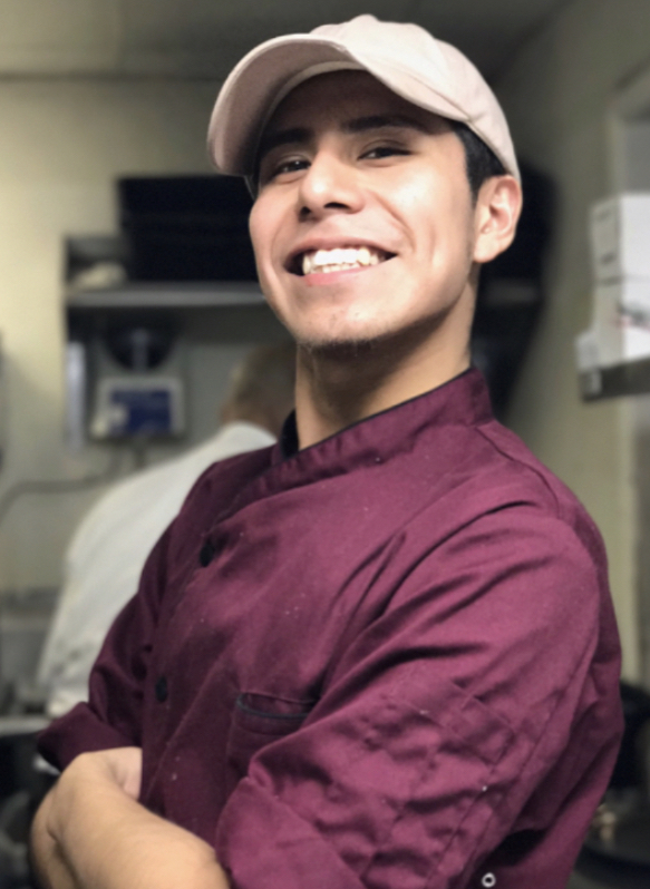 Erick smiles at the camera, wearing his chef uniform.