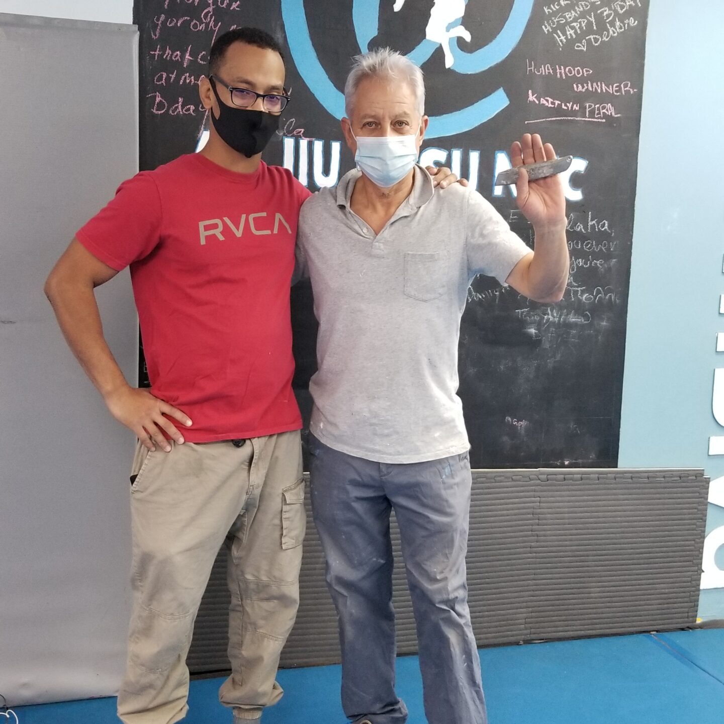 Alvaro and his father stand in front of the AT Jiu Jitsu NYC sign in the studio.